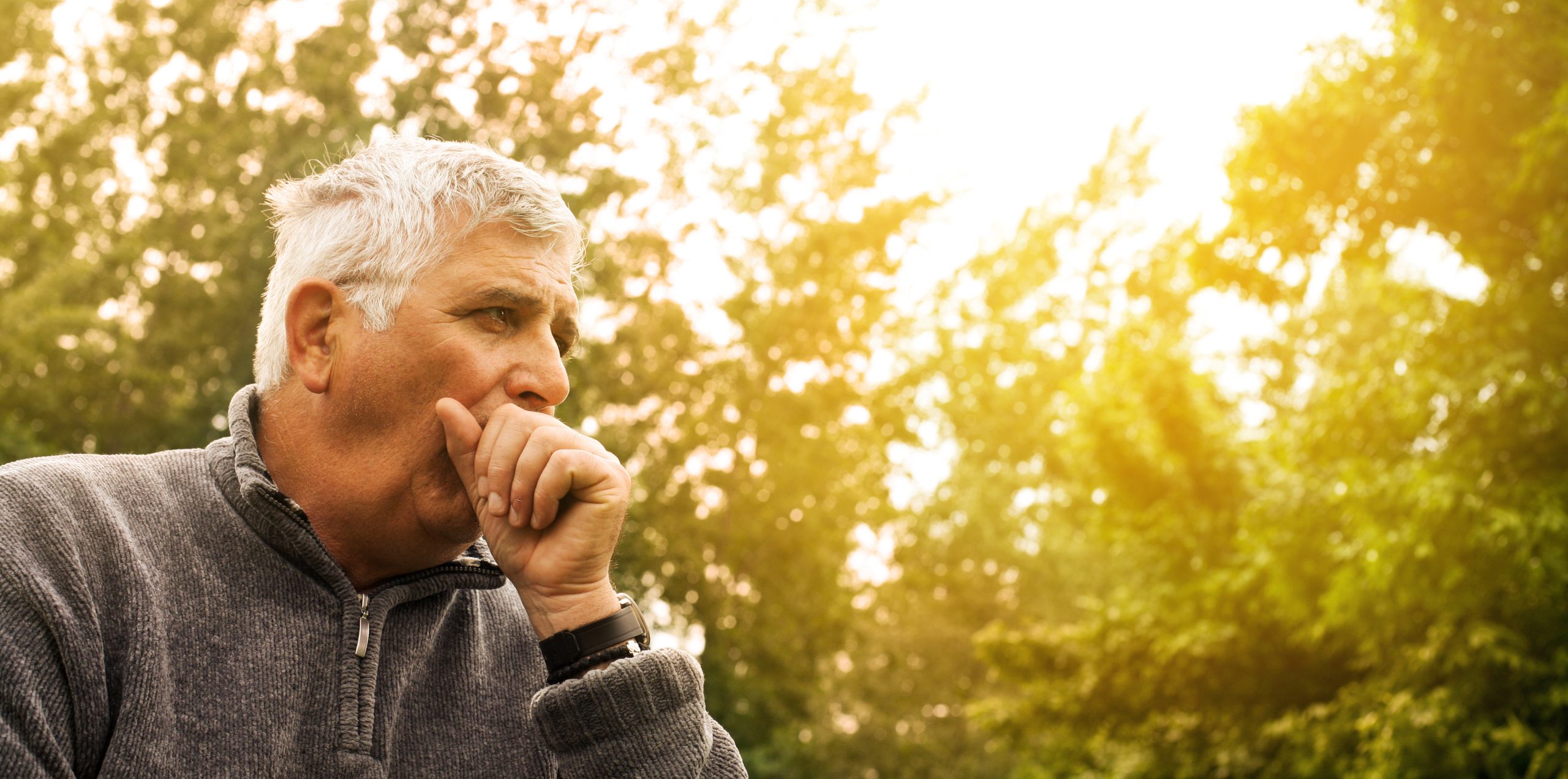 Elderly man suffering from chronic cough while outdoors. 