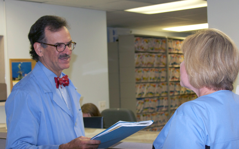 Dr. Mandel Sher in a blue lab coat speaking to a patient about chronic cough.